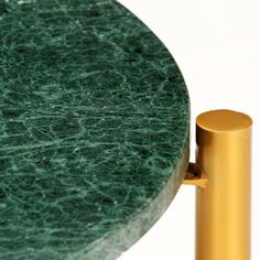 a green marble topped table with a gold metal post on the side and a white wall behind it