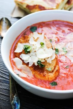 a bowl of tomato soup with bread and parmesan cheese on the side, ready to be eaten