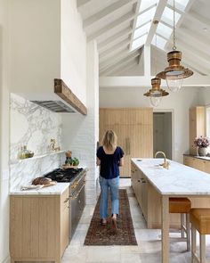 a woman is standing in the middle of a kitchen with white marble countertops and wooden cabinets