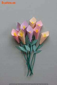 flowers made out of paper sitting on top of a gray surface with green stems in the foreground