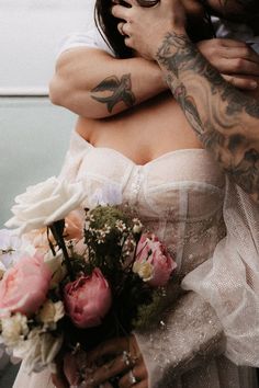 a man and woman hugging each other with tattoos on their arms, both holding flowers