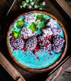 a bowl filled with berries and kiwis on top of a wooden table next to flowers