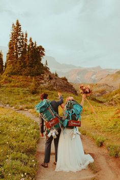 a bride and groom walking down a path in the mountains with their backpacks on