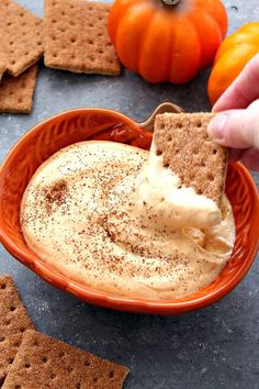 a person dipping some kind of food in a bowl with crackers on the side