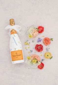 a bottle of wine next to flowers and petals on a white surface with the letter a