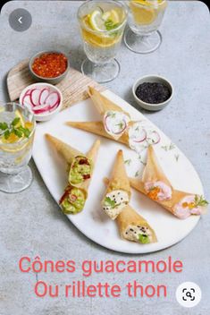 an assortment of appetizers on a plate with glasses and condiments in the background