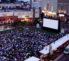 an overhead view of people sitting on the grass in front of a movie screen at night