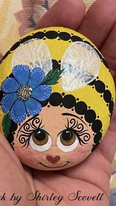 a hand holding a painted rock with a flower on it