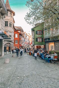 people are walking down the street in front of shops and restaurants on cobblestone streets