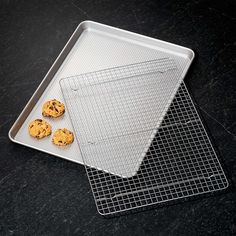 three cookies sitting on top of a cookie sheet next to a cooling rack with one cookie in it