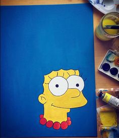 a drawing of the simpsons is shown on a blue paper next to some paintbrushes