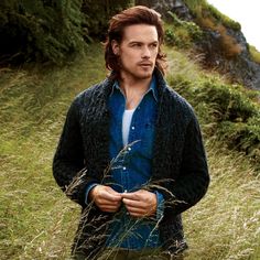 a man standing in tall grass with the caption saying, wearing a cardigan still hot