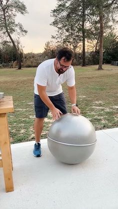 a man is doing something with a large metal ball on the ground in front of him