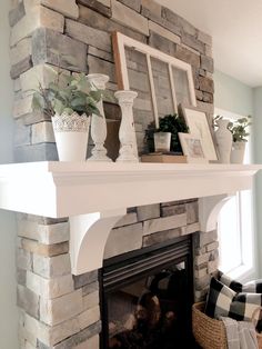 a fireplace with some potted plants and pictures on it's mantle above the fire place