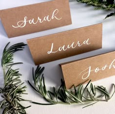 three place cards sitting on top of a table next to some greenery and leaves