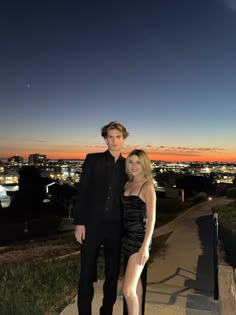 a man and woman posing for a photo in front of the city at night time