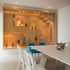 a dining room table with blue chairs and shelves in the wall behind it that are filled with figurines