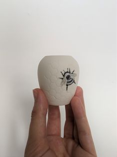 a hand holding a small white object with a bee on it