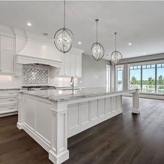 a large kitchen with an island in the middle and three lights hanging from the ceiling