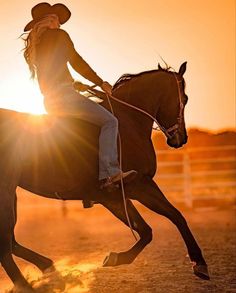 a woman riding on the back of a brown horse in an arena at sundown