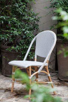 a white wicker chair sitting in front of some potted plants