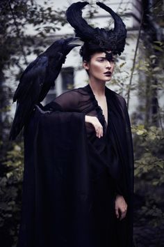 a woman wearing a black cape with two crows on it's head and one bird perched on her shoulder