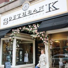 a woman walking past a store front with flowers on it