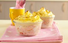 two cups filled with food sitting on top of a pink table cloth next to a yellow cup