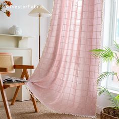 a pink curtain hanging from the side of a window next to a chair and potted plant