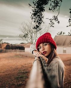 a woman wearing a red hat leaning on a fence