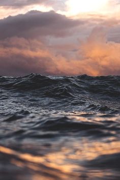 an ocean with waves and clouds in the sky at sunset or dawn, as seen from the water's surface