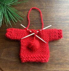 a red knitted sweater ornament hanging from a pine tree with knitting needles