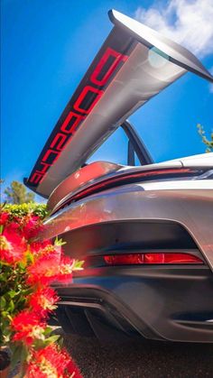 the back end of a silver sports car with its trunk open and flowers in front