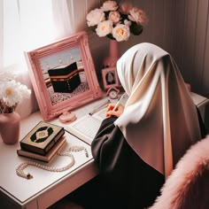 a woman in a hijab sitting at a desk with a laptop and flowers