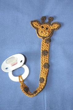 a crocheted giraffe is next to a pacifier on a blue background