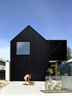 a person kneeling down next to a dog in front of a black building with large windows