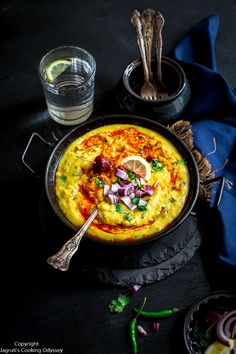 an omelet with onions and herbs in a pan on a black table next to silverware