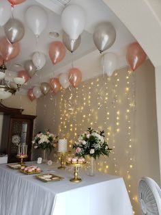 a table topped with lots of white and pink balloons next to a wall covered in lights