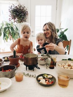 a woman and two children sitting at a table with food