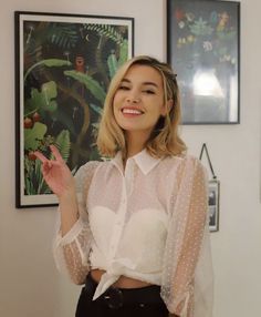 a woman in a white shirt and black skirt standing next to a wall with pictures on it