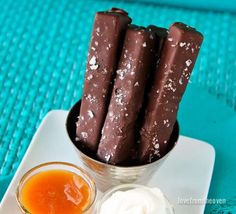 there are three chocolate sticks in a small bowl on the plate next to some dipping sauce