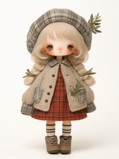 a doll wearing a coat and hat with green leaves on it's head, standing in front of a white background