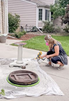 a woman using a power drill to fix a hole in the sidewalk outside her house