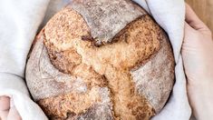 a person holding a loaf of bread on top of a white cloth in their hands