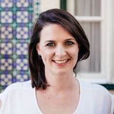 a smiling woman in front of a blue and white tile wall with green shutters