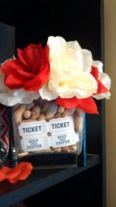 there is a vase with flowers and tickets on the shelf next to some candy bars