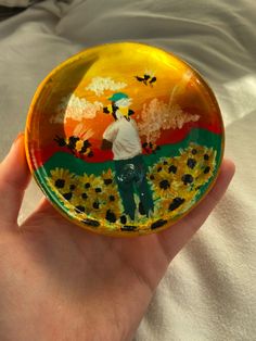 a hand holding a small glass plate with a painting on it's front and side