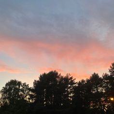 the sun is setting over some trees and grass in front of a blue sky with pink clouds