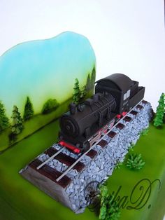 a cake with a train on the tracks in front of trees and rocks, is ready to be eaten