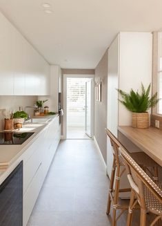 a long narrow kitchen with white cabinets and counter tops, along with bar stools